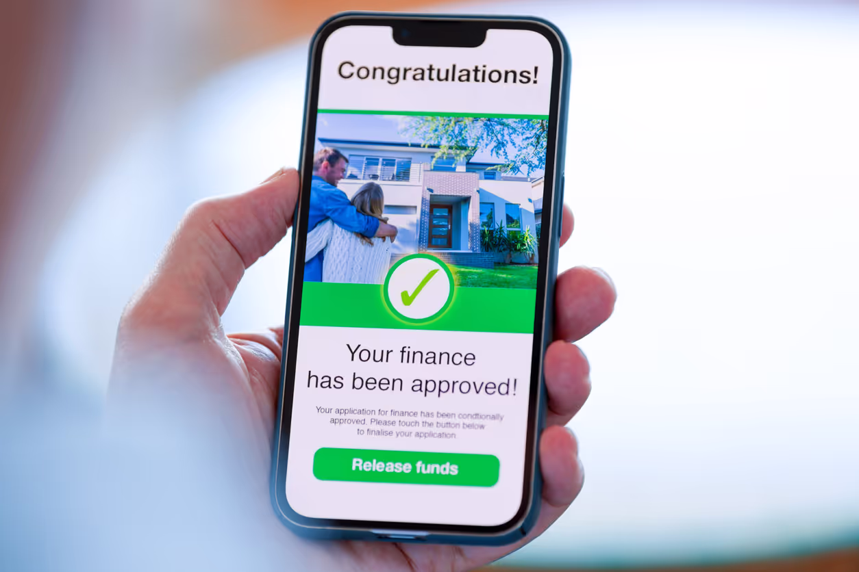 A smartphone displays a "Congratulations!" message, indicating that a user's finance has been approved. The screen shows a happy couple in front of their new house with a green checkmark, followed by a "Release funds" button. The image highlights a successful loan or mortgage application.
