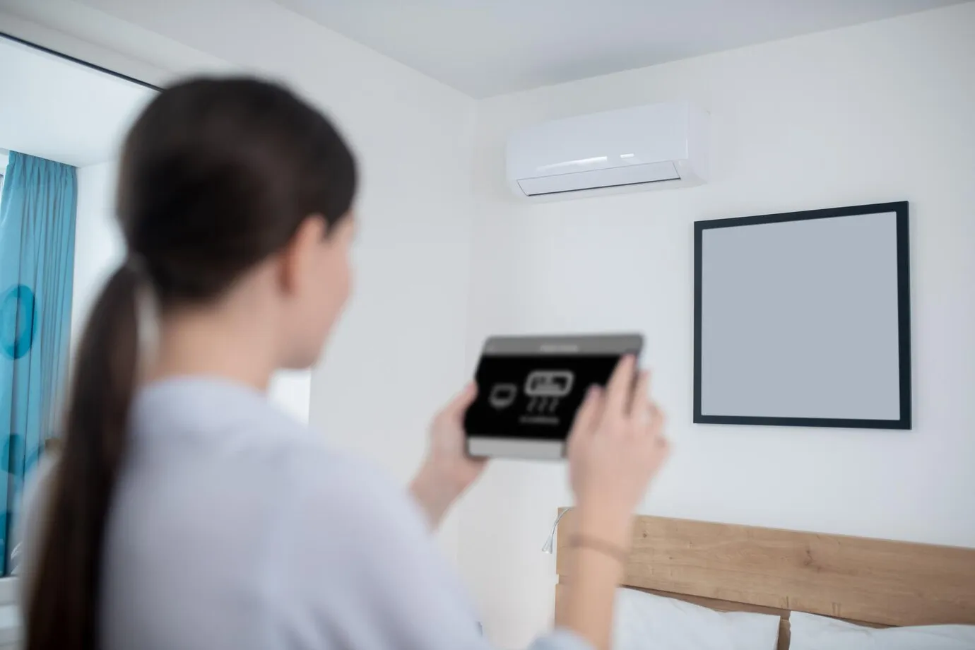Person adjusting air conditioning remote control near wall-mounted unit