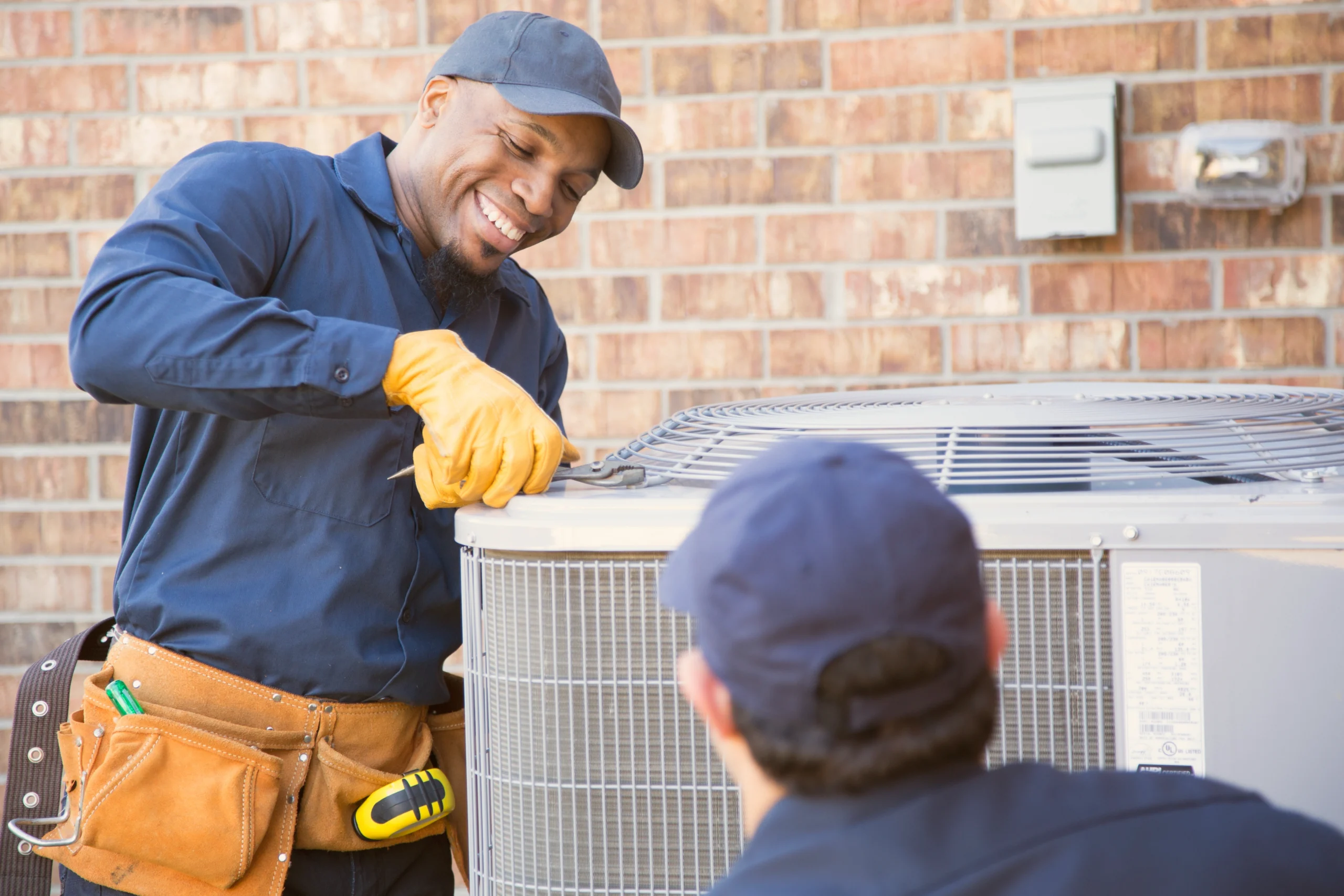 Two mens are repairing an air conditioner together in a well-lit room.