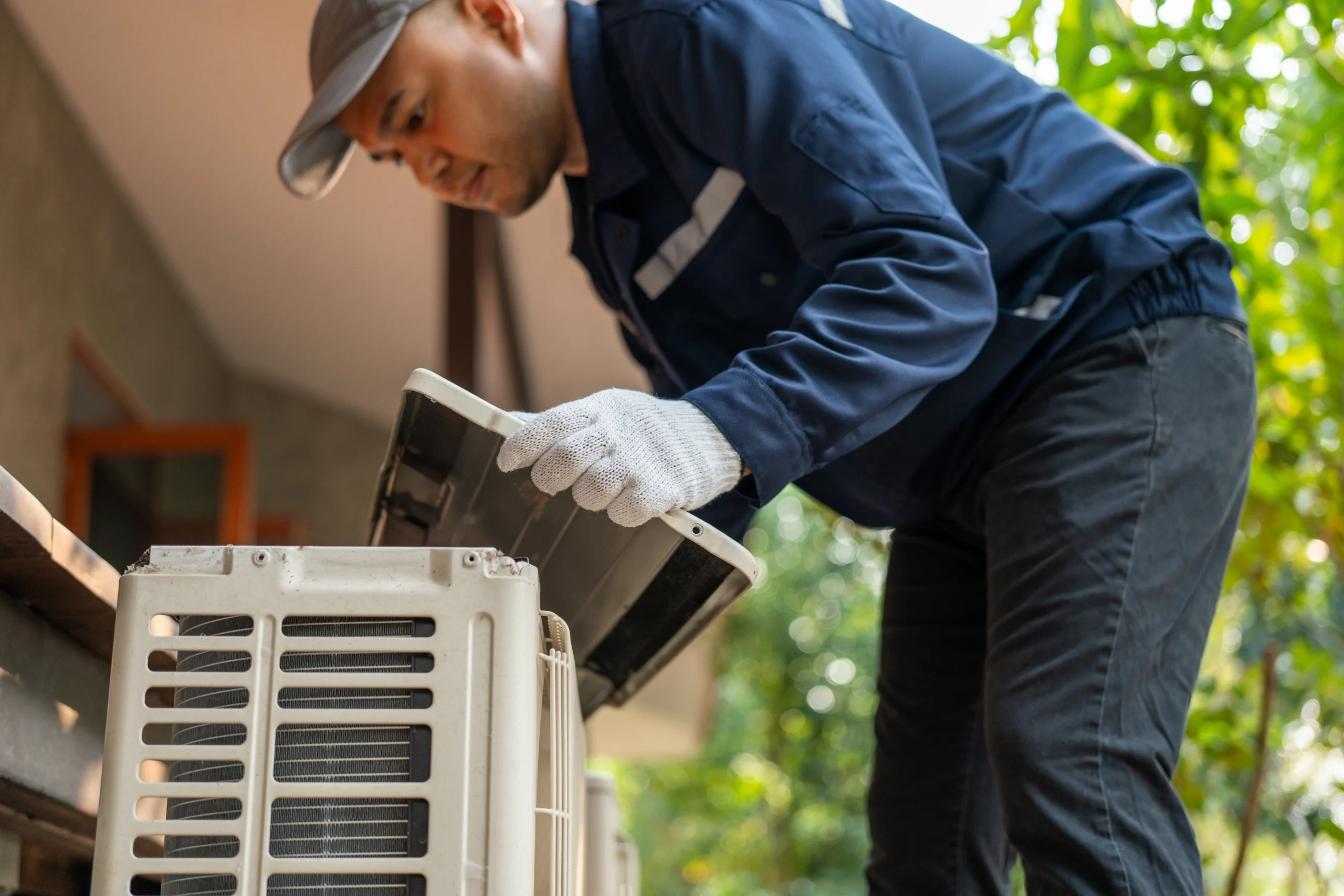 Man in a blue uniform and cap repairs an outdoor air conditioning unit, focus on his work 