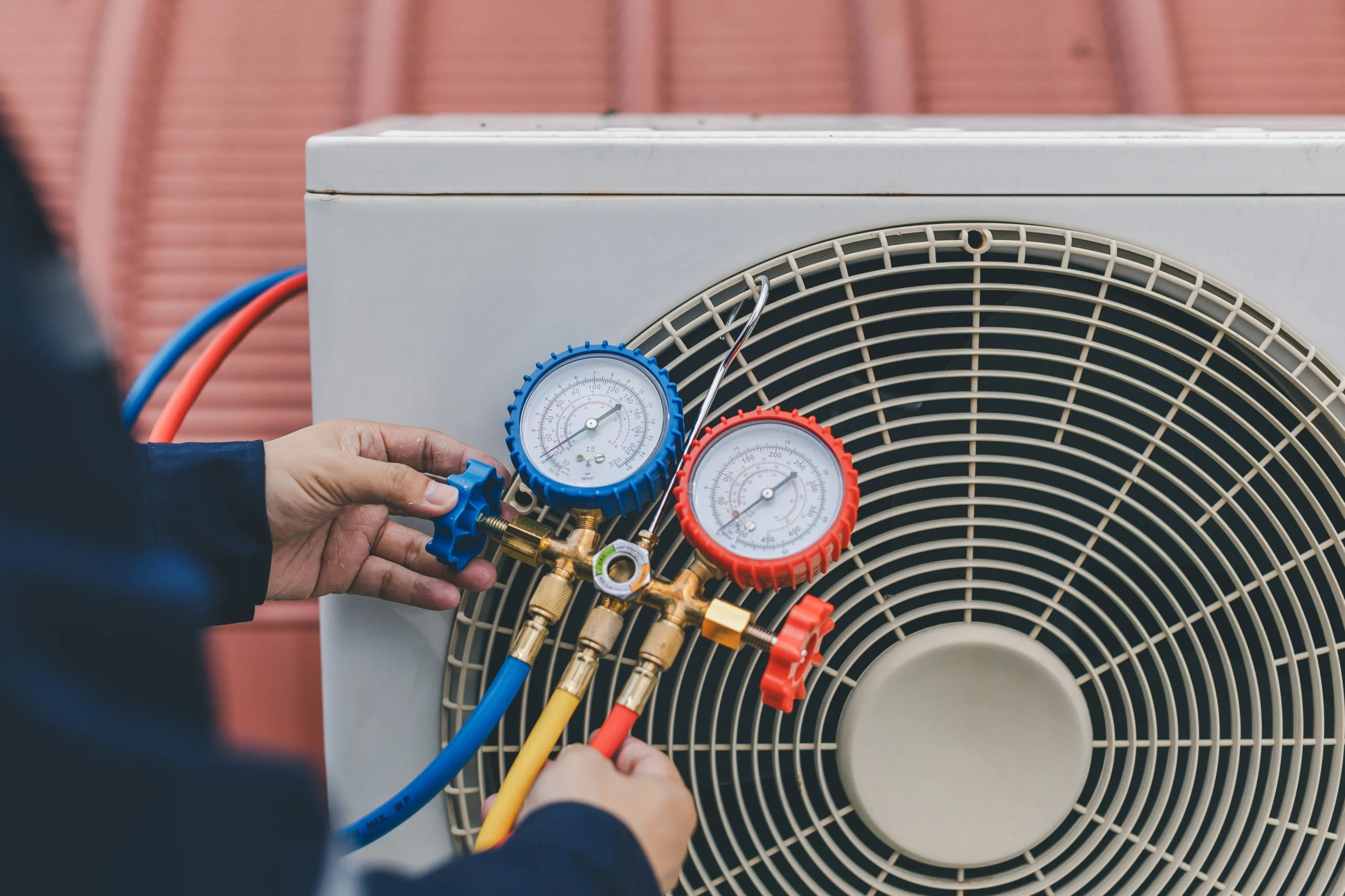 A person adjusts a blue and red pressure gauge connected to an air conditioning unit. 
